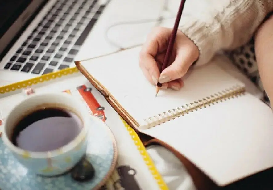 A person writing or sketching in a journal on a beautifully styled desk.